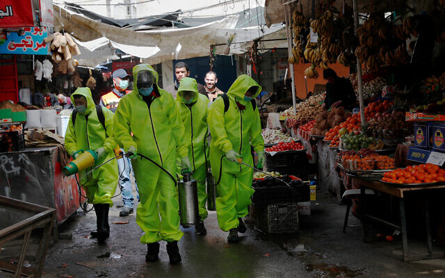 Workers in protective gear spray disinfectant at the main market in Gaza City on March 27. Photo: AP/Adel Hana