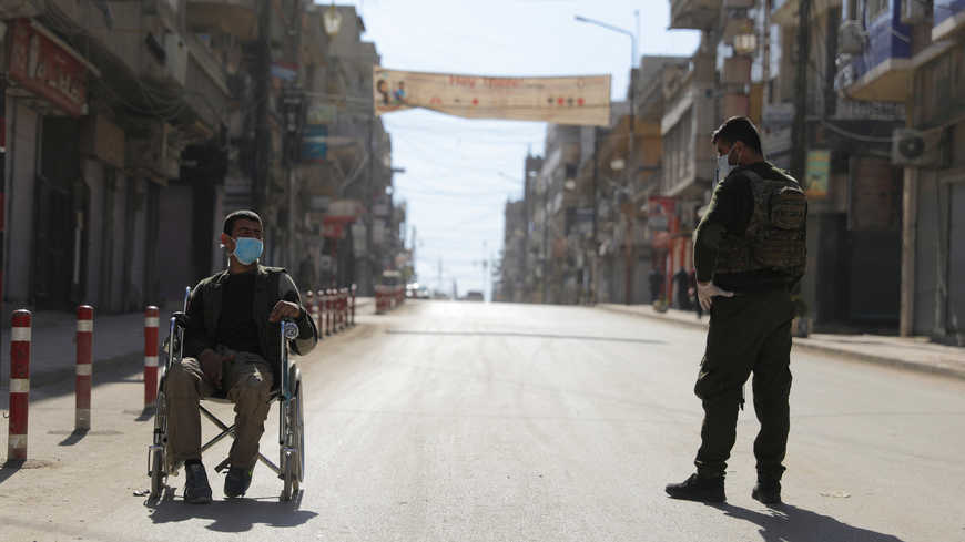 A member of the Kurdish-led Asayish security organisation stands near a man in a wheelchair along an empty street, as coronavirus restrictions are imposed in Qamishli, Syria