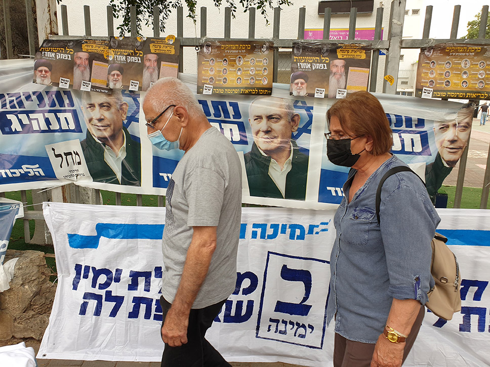 Israeli voters walking by political posters and slogans outside an election polling station in Holon, Israel, 23 March 2021. (Credit: Roman Yanushevsky/Shutterstock)