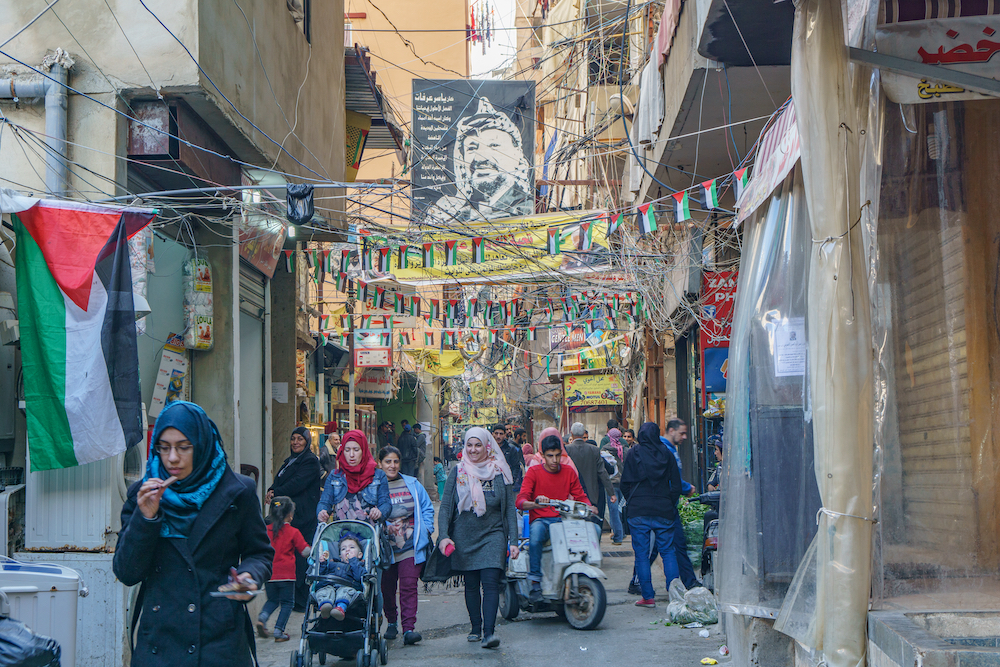 Palestinians walking under the poster of Yasser Arafat in Sabra and Shatila refugee camp in Beirut, Lebanon (Credit: Shutterstock)