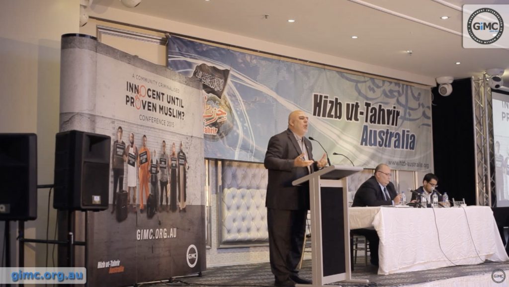 HT Australia leader Ismai’l al-Wahwah speaking at the Nov. 2015 “Innocent Until Proven Muslim?” conference in Melbourne. Behind him is the HT Australia banner (YouTube screenshot)