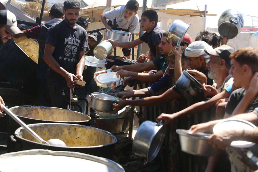 Displaced Palestinians receive food in Al-Mawasi, west of Khan Younis city in the southern Gaza Strip (Image: Anas Mohammed/ Shutterstock)
