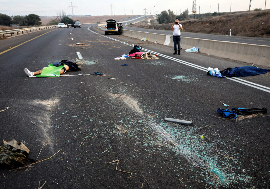 A man takes a photo of murder victims strewn across a road following a mass-infiltration by Hamas gunmen from the Gaza Strip, in the Sderot area, southern Israel, October 7, 2023 (Image: Reuters/Ammar Awad/ AAP)