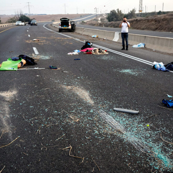 A man takes a photo of murder victims strewn across a road following a mass-infiltration by Hamas gunmen from the Gaza Strip, in the Sderot area, southern Israel, October 7, 2023 (Image: Reuters/Ammar Awad/ AAP)