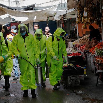 Workers in protective gear spray disinfectant at the main market in Gaza City on March 27. Photo: AP/Adel Hana