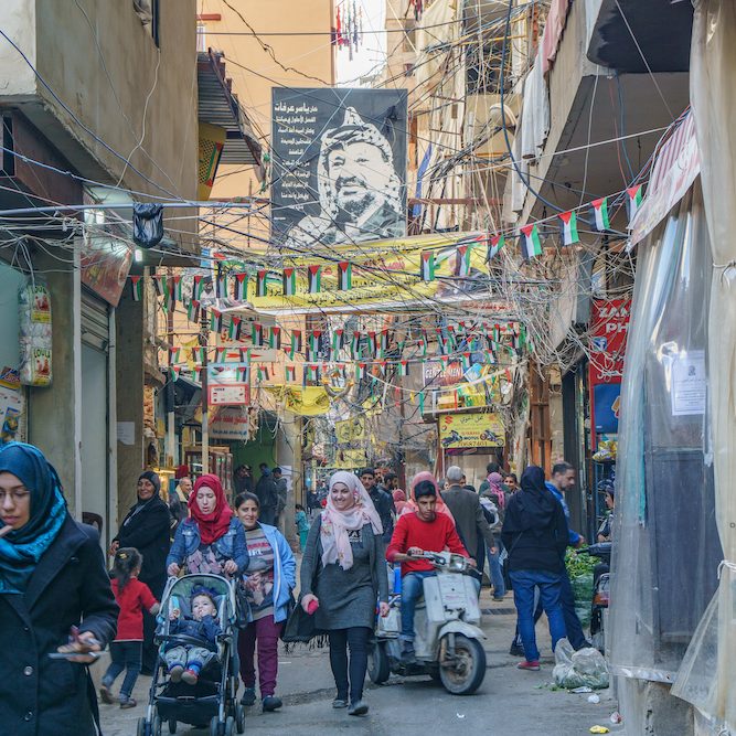 Palestinians walking under the poster of Yasser Arafat in Sabra and Shatila refugee camp in Beirut, Lebanon (Credit: Shutterstock)